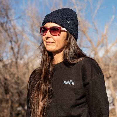 close up of snek cycling crewneck fleece sweatshirt on female model wearing a blue knit lumber jack snek beanie
